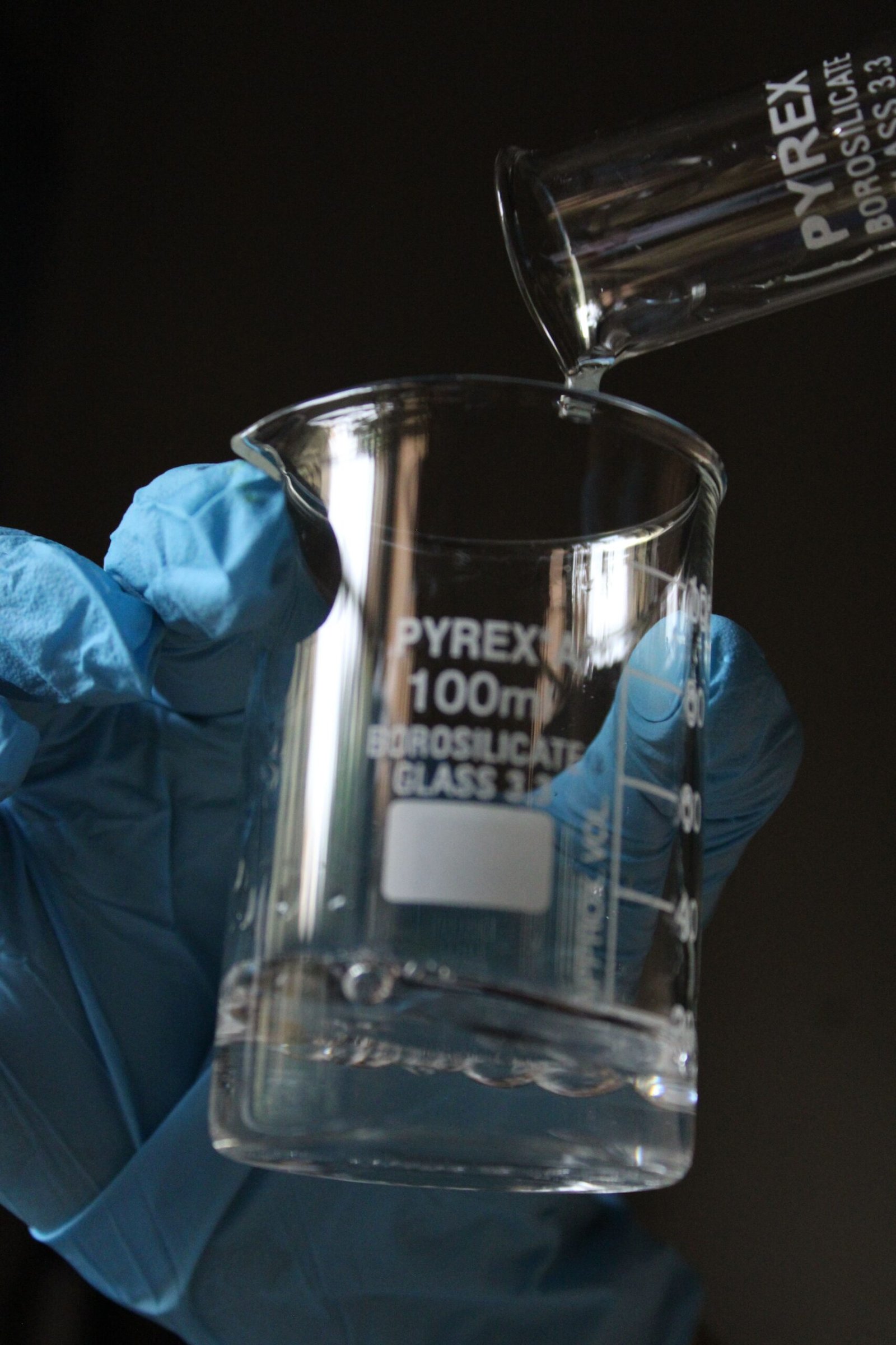 Close-up of liquid pouring into a 100ml lab beaker, showcasing laboratory equipment in use.