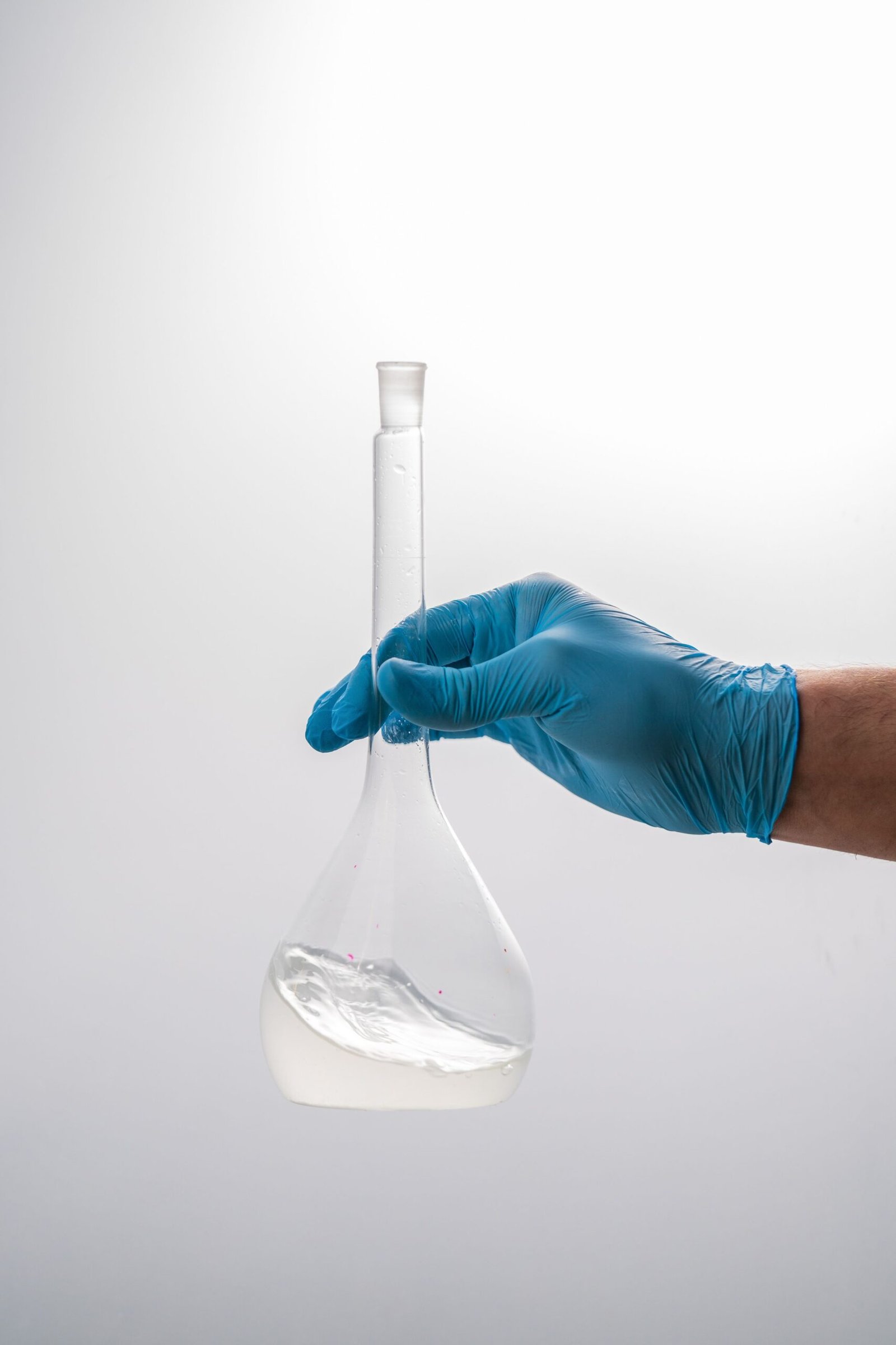 Close-up of a gloved hand holding a volumetric flask in a scientific laboratory setting.